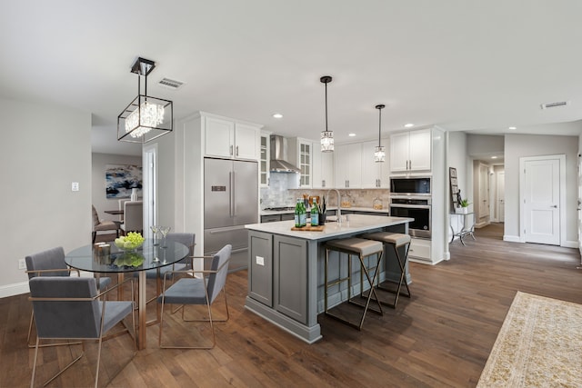 kitchen with white cabinetry, wall chimney range hood, built in appliances, decorative backsplash, and dark hardwood / wood-style floors