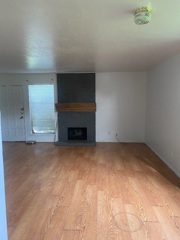 unfurnished living room with a textured ceiling, a large fireplace, and light wood-type flooring