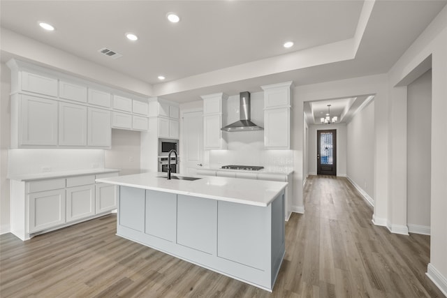 kitchen featuring wall chimney exhaust hood, light hardwood / wood-style floors, a center island with sink, and stainless steel microwave