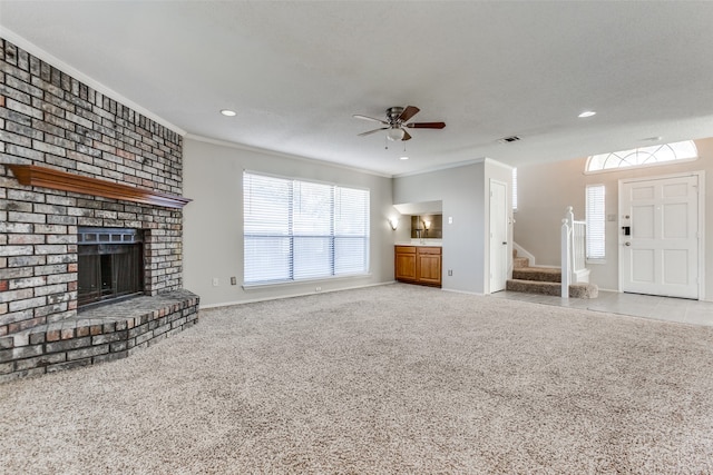 unfurnished living room featuring a textured ceiling, light colored carpet, a brick fireplace, ornamental molding, and ceiling fan