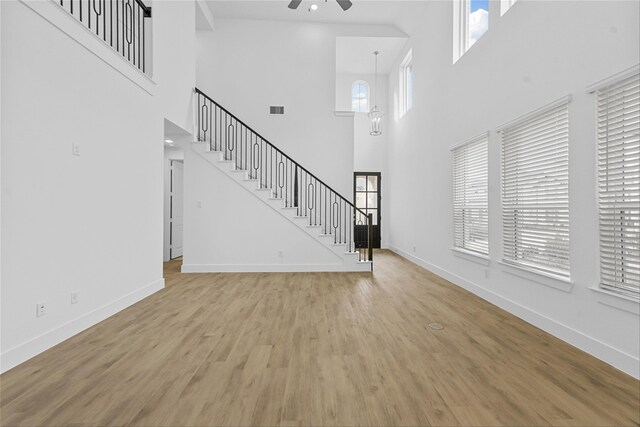 unfurnished living room with ceiling fan with notable chandelier, a wealth of natural light, and light wood-type flooring