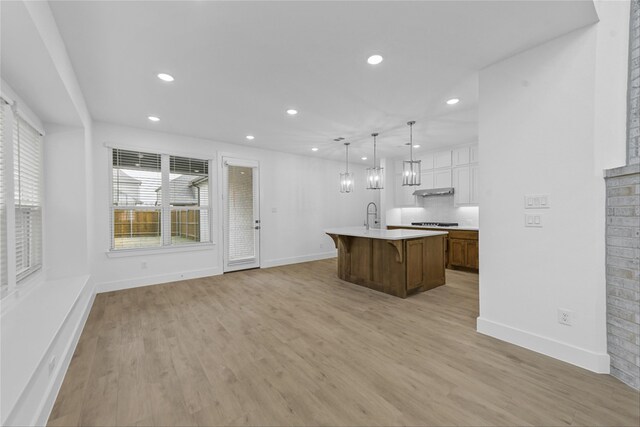 kitchen with hanging light fixtures, white cabinetry, a center island with sink, and light wood-type flooring