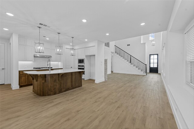 kitchen with white cabinetry, stainless steel microwave, light hardwood / wood-style floors, decorative light fixtures, and a large island with sink