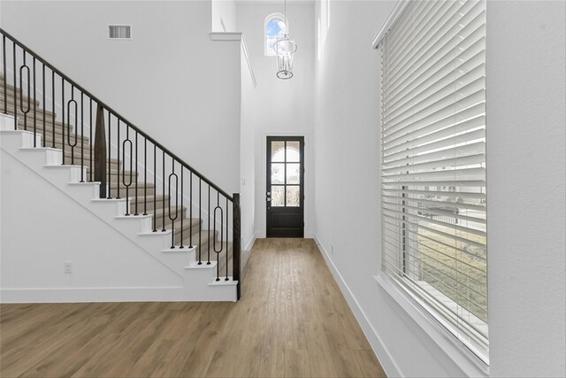 entrance foyer with a towering ceiling, wood-type flooring, and a notable chandelier