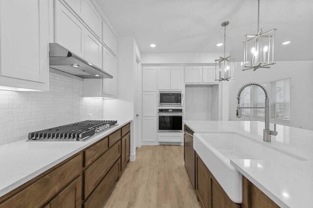 kitchen featuring decorative light fixtures, ventilation hood, white cabinetry, sink, and stainless steel appliances