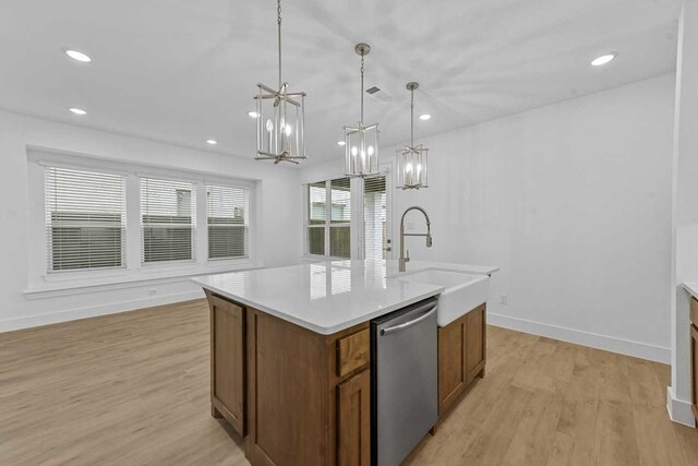 kitchen featuring dishwasher, an island with sink, sink, hanging light fixtures, and light wood-type flooring