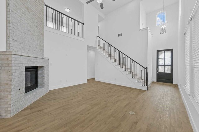 unfurnished living room with ceiling fan with notable chandelier, hardwood / wood-style floors, and a brick fireplace