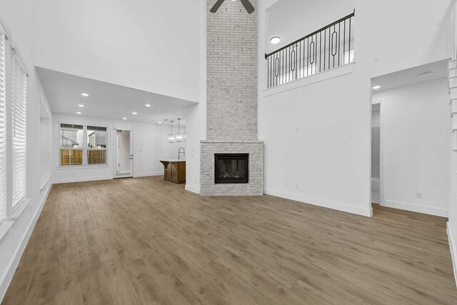 unfurnished living room featuring hardwood / wood-style flooring, ceiling fan, a fireplace, and a towering ceiling