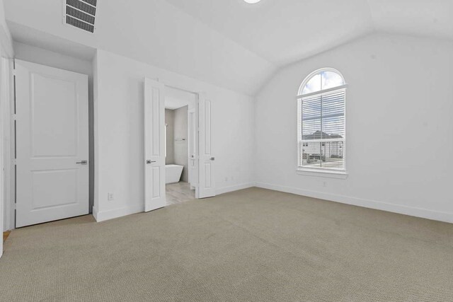 unfurnished bedroom with ensuite bathroom, lofted ceiling, and light carpet