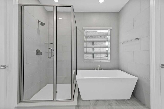 bathroom with shower with separate bathtub and tile walls