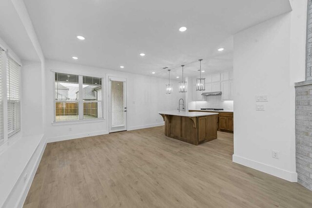 kitchen featuring white cabinetry, a kitchen island with sink, light wood-type flooring, and decorative light fixtures