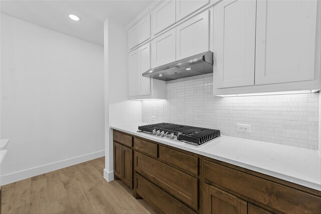 kitchen with stainless steel gas stovetop, white cabinets, backsplash, light wood-type flooring, and wall chimney exhaust hood