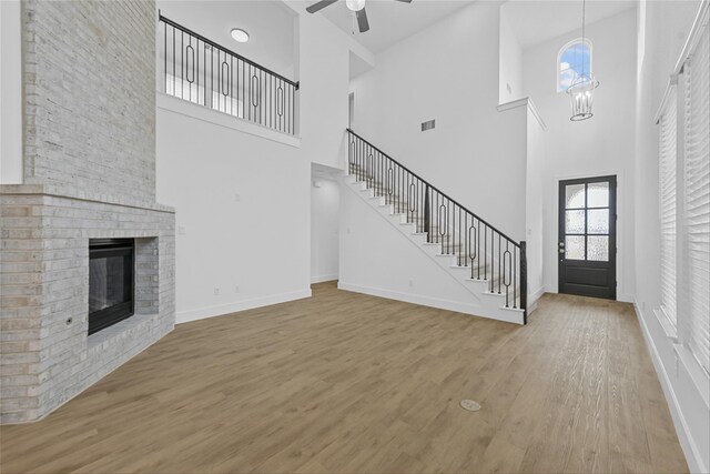 unfurnished living room with wood-type flooring, a fireplace, and ceiling fan with notable chandelier