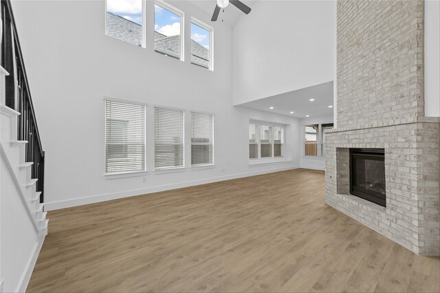 unfurnished living room featuring ceiling fan, a brick fireplace, and light hardwood / wood-style floors