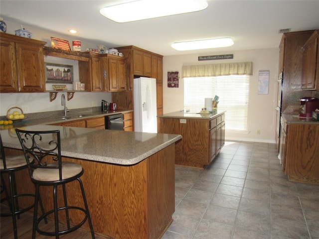 kitchen featuring sink, dark tile flooring, a breakfast bar, dishwasher, and white refrigerator with ice dispenser