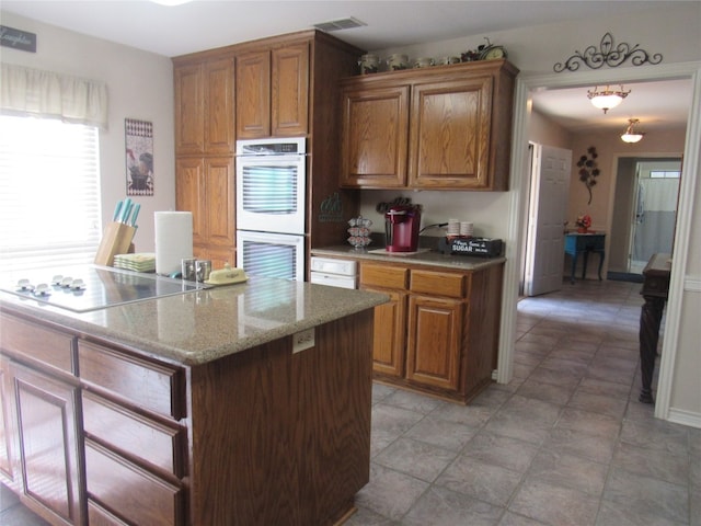 kitchen with double oven, black electric cooktop, light tile floors, and light stone countertops