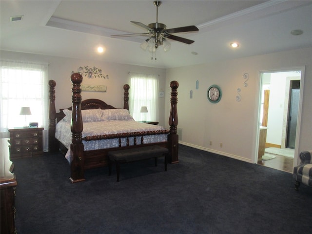 carpeted bedroom with a raised ceiling, multiple windows, ceiling fan, and connected bathroom