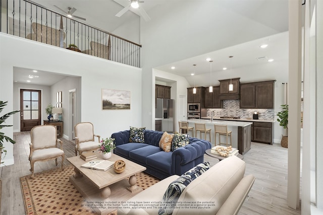 living room featuring ceiling fan, light hardwood / wood-style floors, and a high ceiling