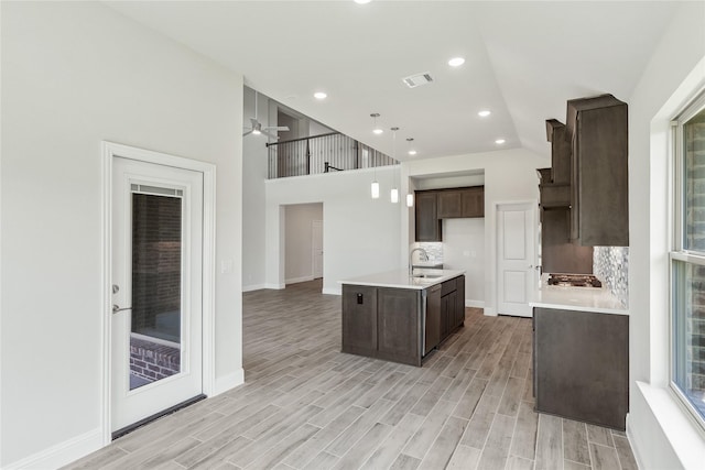 kitchen featuring pendant lighting, backsplash, a kitchen island with sink, light hardwood / wood-style floors, and dark brown cabinetry