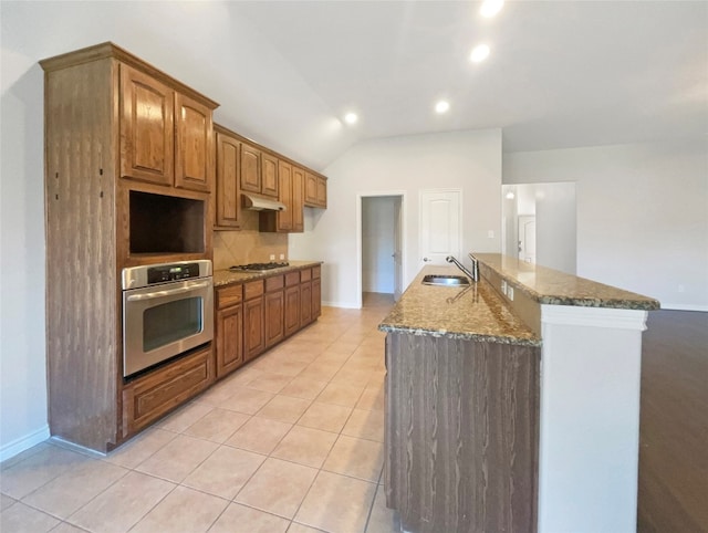 kitchen with appliances with stainless steel finishes, backsplash, dark stone countertops, sink, and a kitchen island with sink