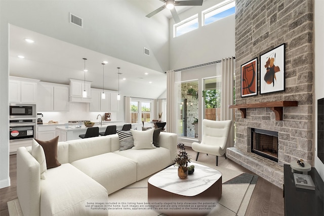 living room featuring a towering ceiling, dark hardwood / wood-style flooring, ceiling fan, sink, and a fireplace