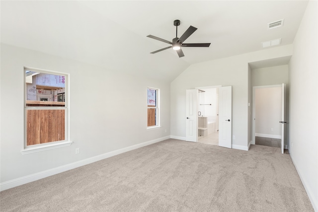 unfurnished bedroom with ceiling fan, vaulted ceiling, light colored carpet, and ensuite bath