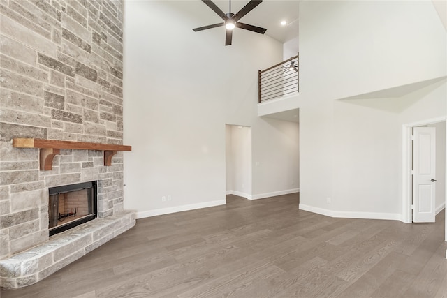 unfurnished living room featuring a towering ceiling, hardwood / wood-style flooring, a stone fireplace, and ceiling fan