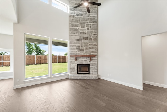 unfurnished living room featuring a fireplace, ceiling fan, dark hardwood / wood-style flooring, and a high ceiling