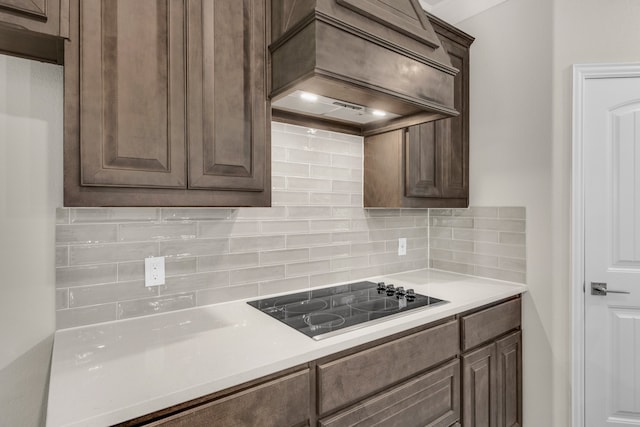 kitchen with dark brown cabinetry, black electric cooktop, custom exhaust hood, and backsplash