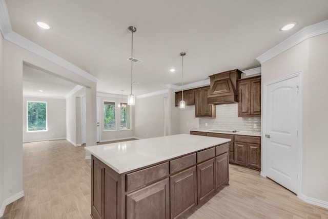 kitchen featuring tasteful backsplash, a center island, premium range hood, decorative light fixtures, and ornamental molding