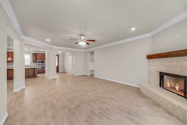 unfurnished living room featuring light hardwood / wood-style floors, a stone fireplace, ceiling fan, and crown molding