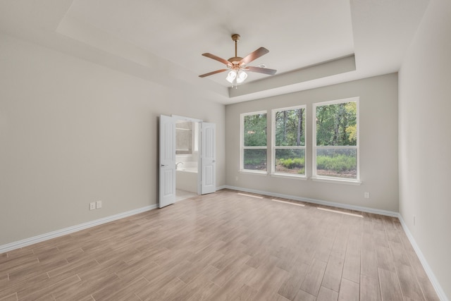 unfurnished room featuring ceiling fan, light wood-type flooring, and a tray ceiling