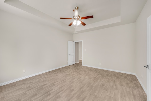 unfurnished room featuring a tray ceiling, light hardwood / wood-style flooring, and ceiling fan