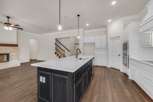 kitchen with white cabinetry, stainless steel appliances, hardwood / wood-style floors, sink, and a stone fireplace