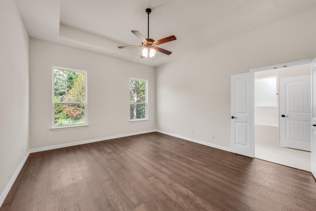 unfurnished room with a raised ceiling, dark hardwood / wood-style floors, and ceiling fan