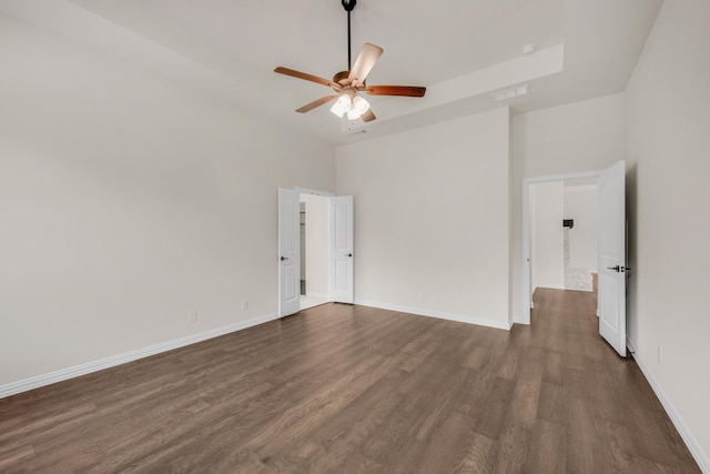 empty room featuring a high ceiling, dark wood-type flooring, and ceiling fan