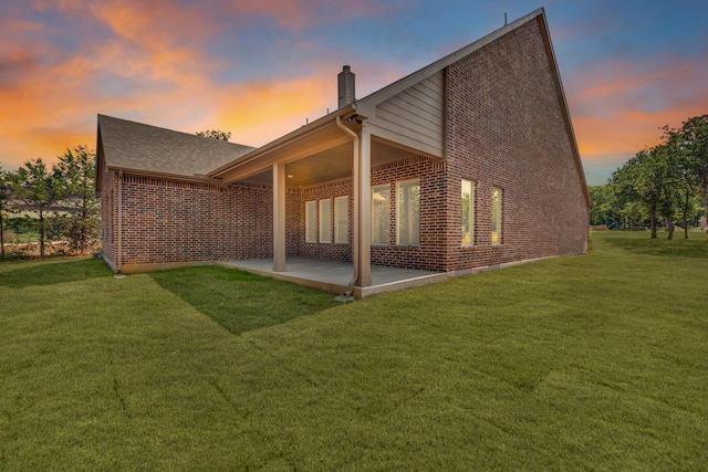 back house at dusk featuring a patio area and a yard