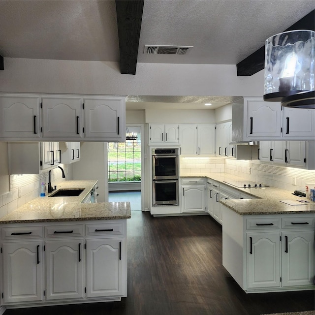 kitchen with double oven, white cabinets, a sink, and a peninsula