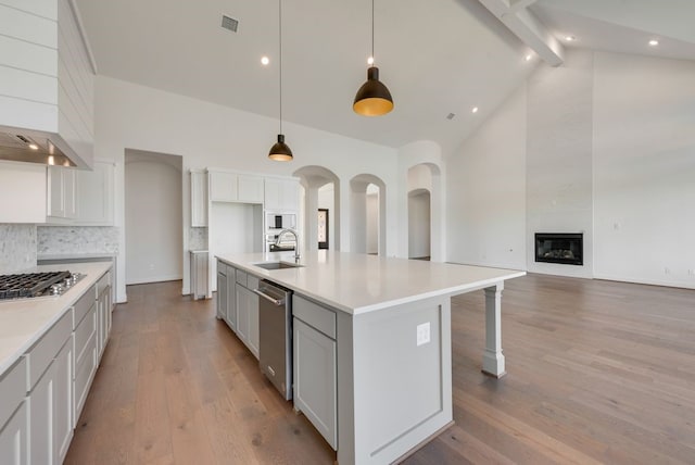 kitchen featuring high vaulted ceiling, a center island with sink, sink, light hardwood / wood-style flooring, and stainless steel appliances