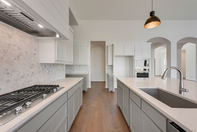 kitchen featuring appliances with stainless steel finishes, custom exhaust hood, sink, decorative light fixtures, and light hardwood / wood-style floors