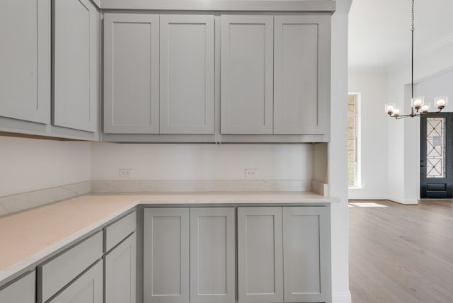 kitchen with gray cabinetry, an inviting chandelier, hanging light fixtures, light wood-type flooring, and ornamental molding