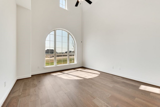 spare room featuring ceiling fan, a healthy amount of sunlight, a high ceiling, and light hardwood / wood-style flooring