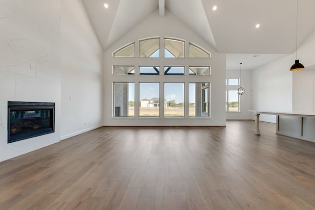 unfurnished living room featuring beamed ceiling, wood-type flooring, high vaulted ceiling, and a tiled fireplace