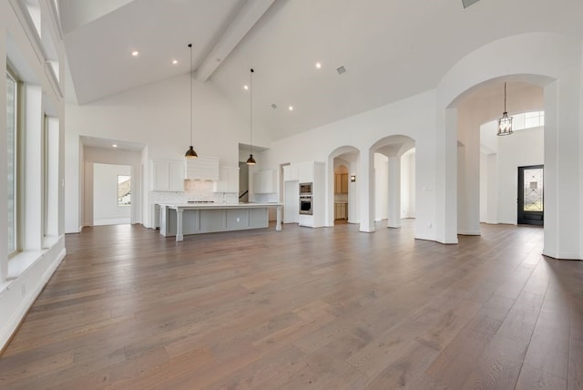 unfurnished living room with a healthy amount of sunlight, dark hardwood / wood-style flooring, beam ceiling, and high vaulted ceiling