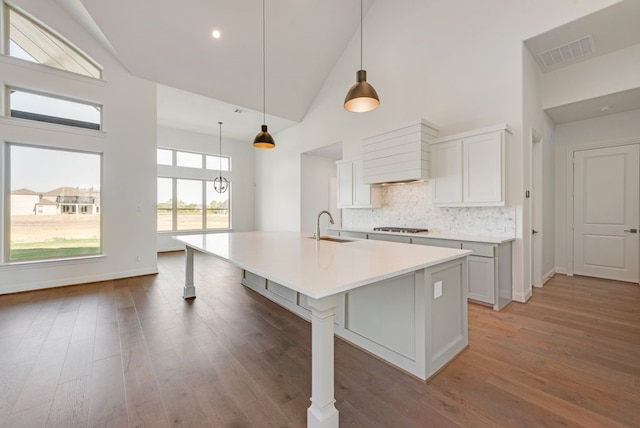 kitchen featuring pendant lighting, a kitchen island with sink, white cabinets, sink, and dark hardwood / wood-style flooring