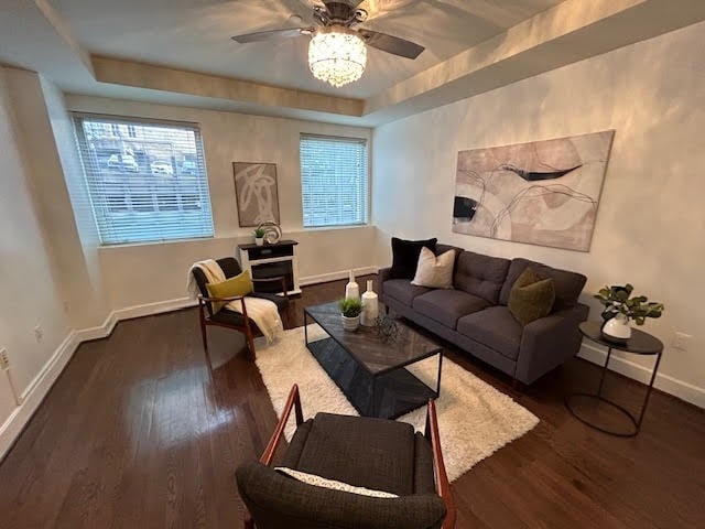 living room with dark wood-type flooring, ceiling fan, and a tray ceiling