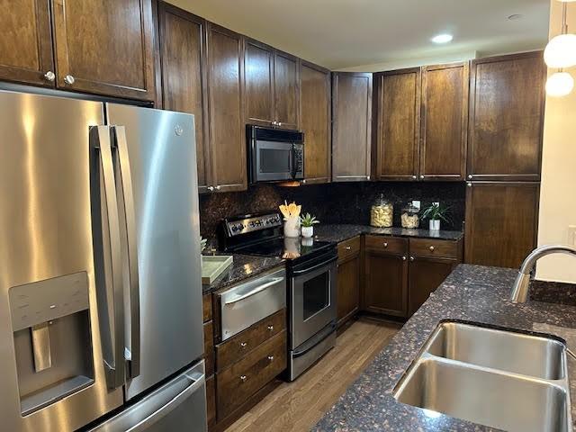 kitchen featuring dark stone countertops, a sink, decorative backsplash, stainless steel appliances, and light wood-type flooring