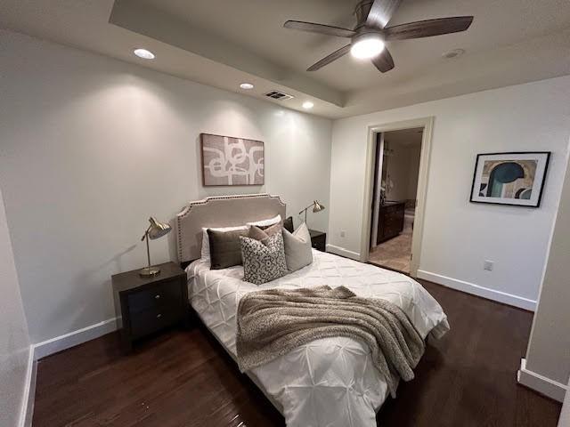 bedroom featuring visible vents, a tray ceiling, baseboards, and wood finished floors