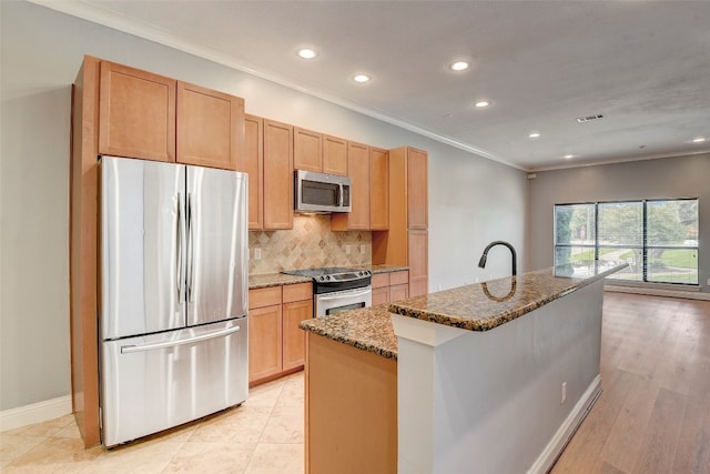 kitchen with appliances with stainless steel finishes, light brown cabinets, backsplash, dark stone countertops, and a kitchen island with sink