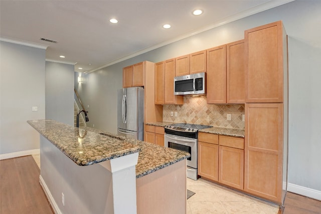 kitchen with appliances with stainless steel finishes, light brown cabinetry, tasteful backsplash, dark stone counters, and an island with sink